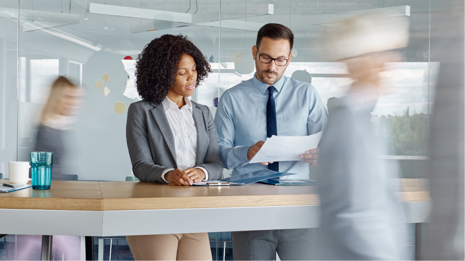/_cms/webroot/Two business people are standing at a table and reading a document together.